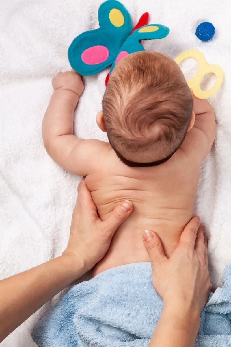 Baby liegt auf dem Bauch und wird sanft am Rücken massiert, daneben ein Schmetterlings-Spielzeug