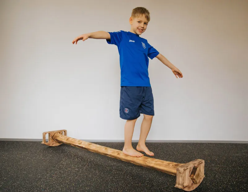 Junge balanciert barfuß über einen hölzernen Balancierbalken