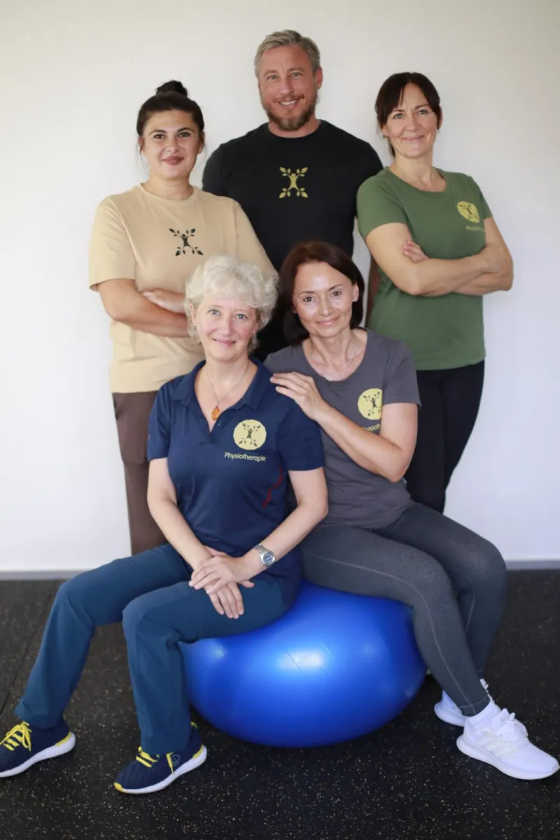 Das Team der Praxis Pravilo Klaus: fünf Mitarbeiterinnen und Mitarbeiter mit einem blauen Gymnastikball