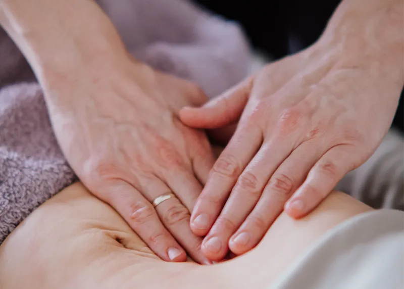 Hände liegen übereinander sanft auf dem Bauch einer Patientin während der viszeralen Behandlung
